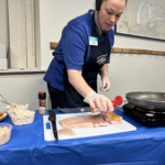 A woman seasons pieces of fish on a cutting board in front of her.